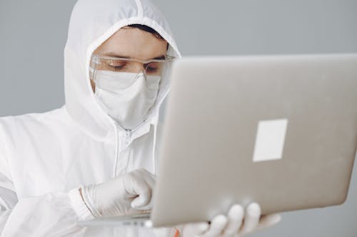Photo of Person in Personal Protective Equipment Using MacBook