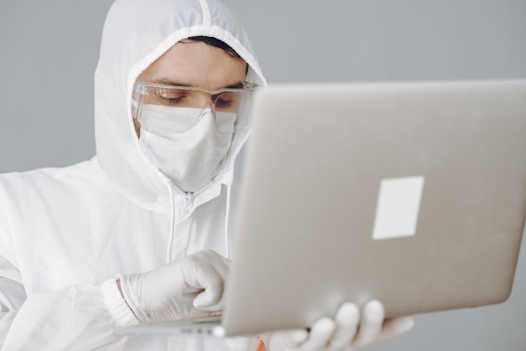 Photo Of Person In Personal Protective Equipment Using MacBook