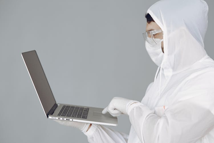 Photo Of Person In Personal Protective Equipment Using MacBook