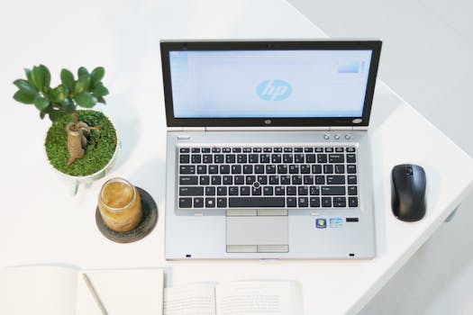 Aerial view of a modern workspace featuring a laptop, plant, and iced coffee in a minimalist setting.