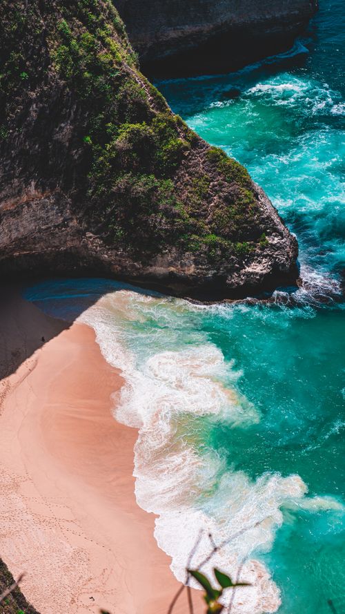Free From above breathtaking view of rough mossy cliffs and sandy beach washed by blue foamy sea waves on tropical island Stock Photo