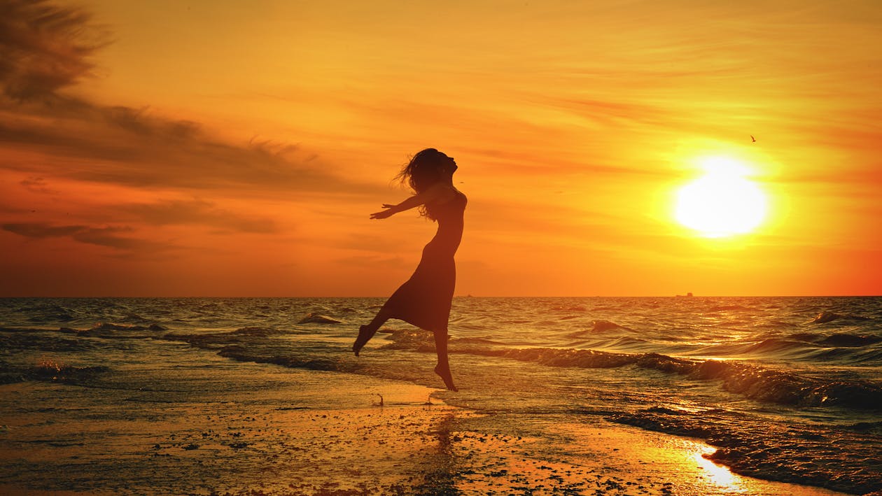 Silhouette of unrecognizable woman jumping above sea beach at sunset ...