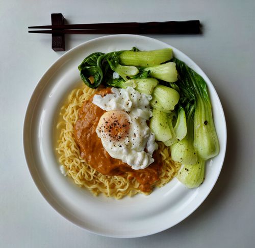 Free Top view of appetizing pasta with red sauce and fried egg on top decorated with ground black pepper near stewed Chinese cabbage and chopsticks Stock Photo