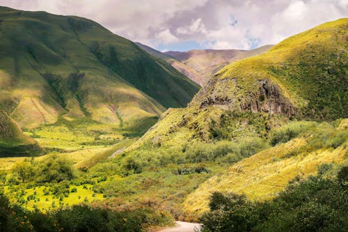 Bright green valley between mountains under cloudy sky in summer