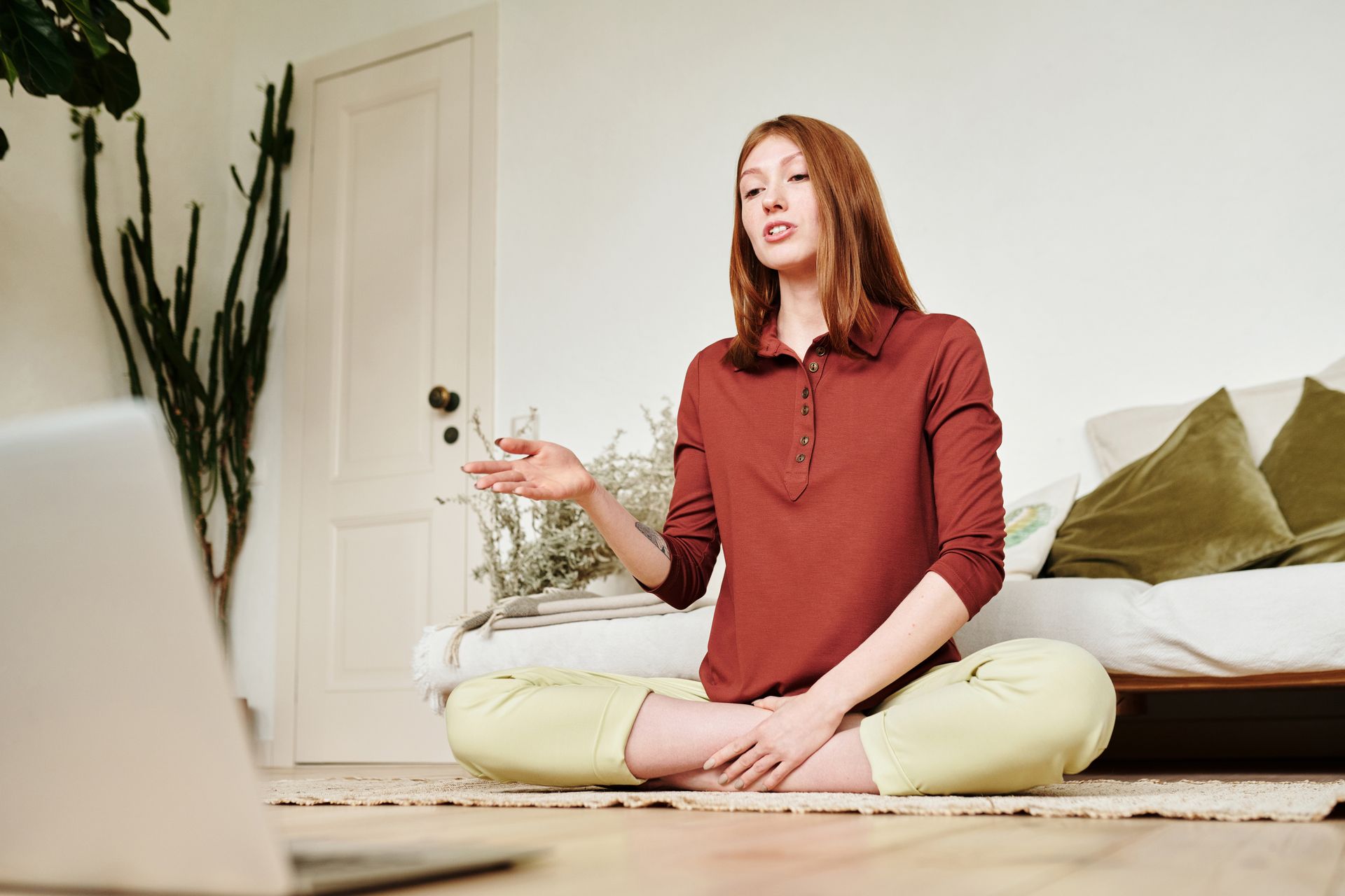 A woman in a lotus position attends an online class from her living room, showcasing modern technology and wellness.