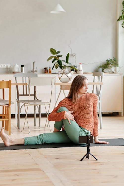 Woman in Orange Sweater and Green Pants Sitting on Black Yoga Mat