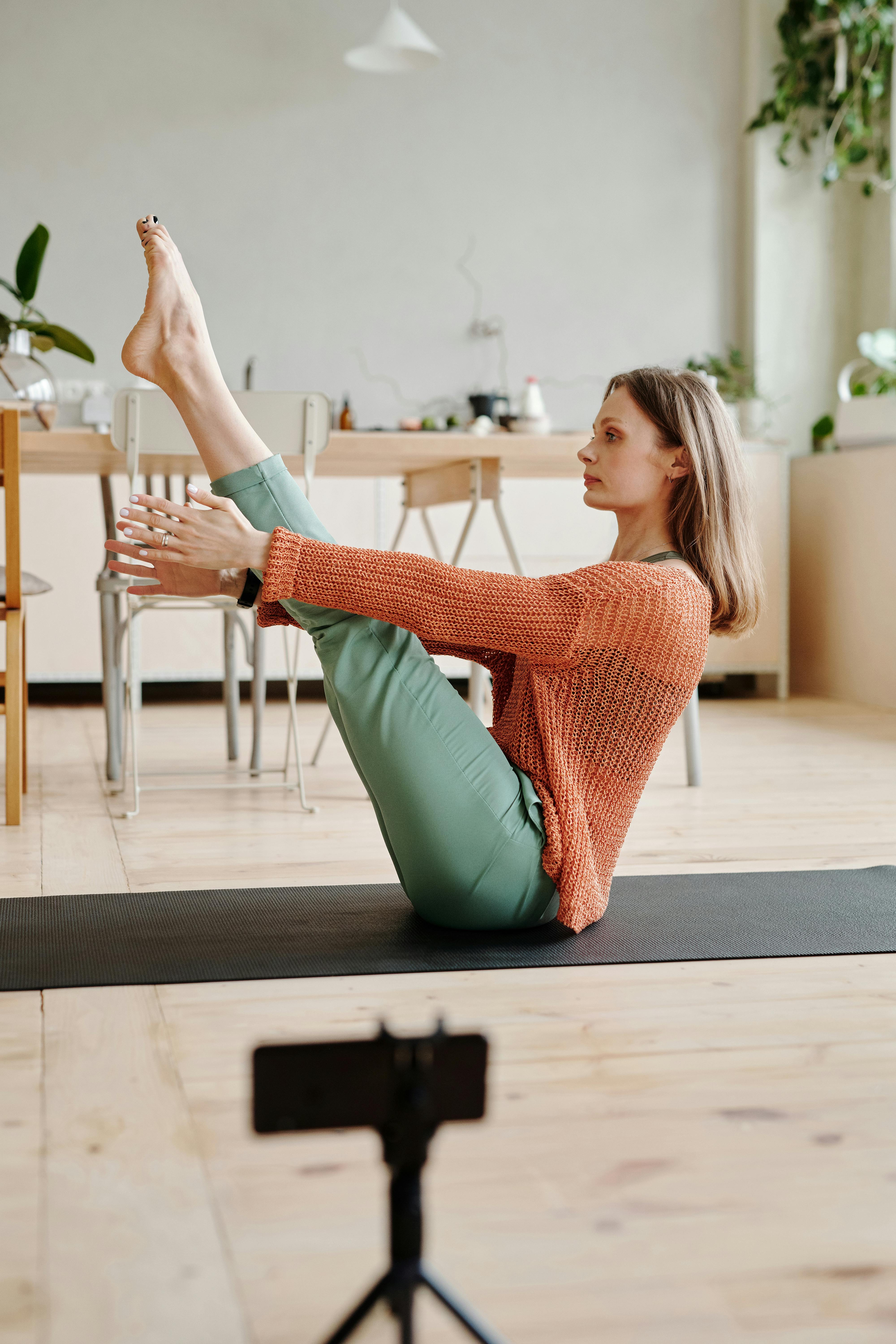 一名女子在室内的垫子上做瑜伽，用智能手机在前景录音