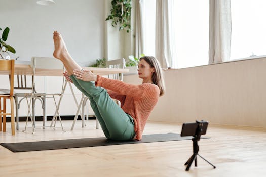 Woman doing a yoga pose indoors, using a smartphone to record or follow along.
