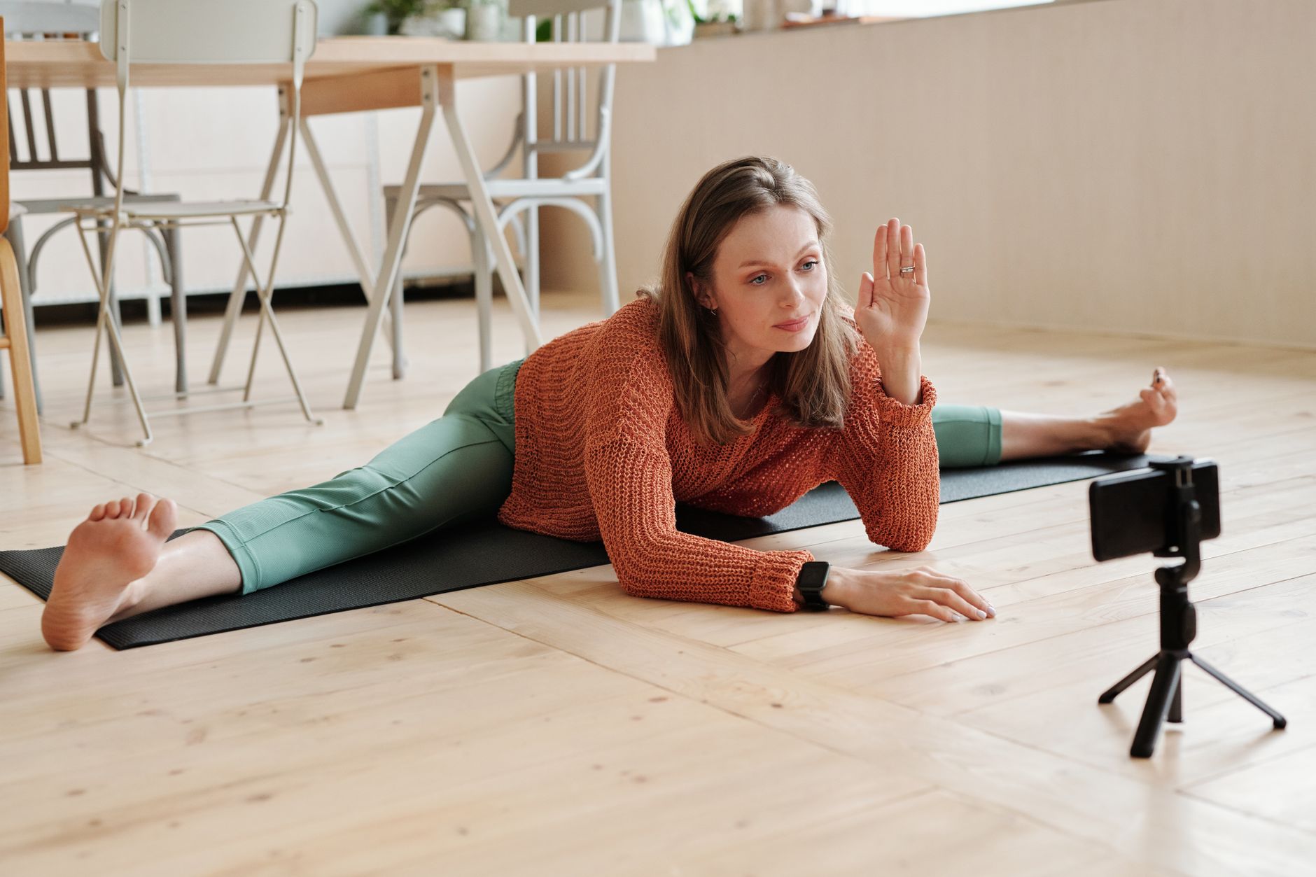 Woman practicing yoga split on video call at home, engaging in a virtual fitness session.