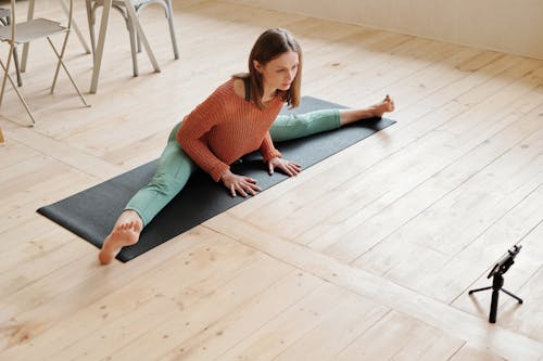 A Woman in Knitted Sweater Doing Leg Split on the Floor in Front of the Mobile Phone