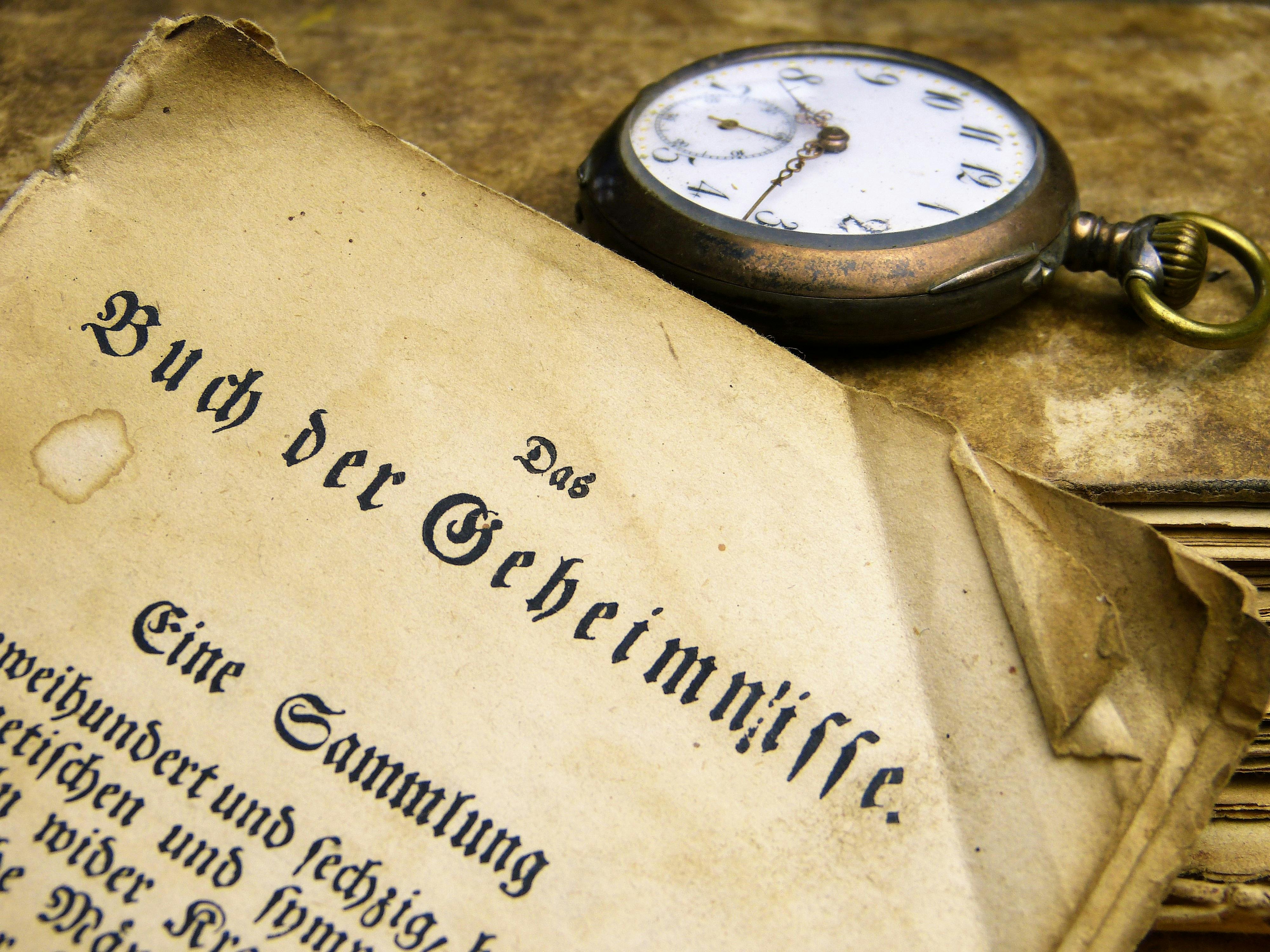 Brass-colored Pocket Watch Beside Book