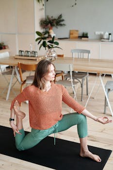Adult woman doing yoga pose on mat in modern kitchen with wooden floor.