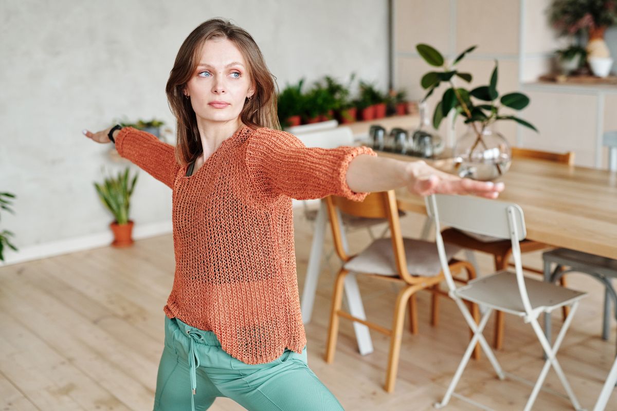 Woman in an orange sweater and teal trousers moving gently at home, showing how everyday activity supports fat loss