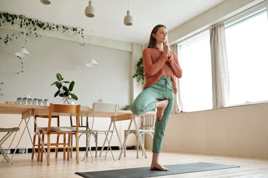 A woman practices yoga on a mat in her sunlit dining room, embracing mindfulness and balance.