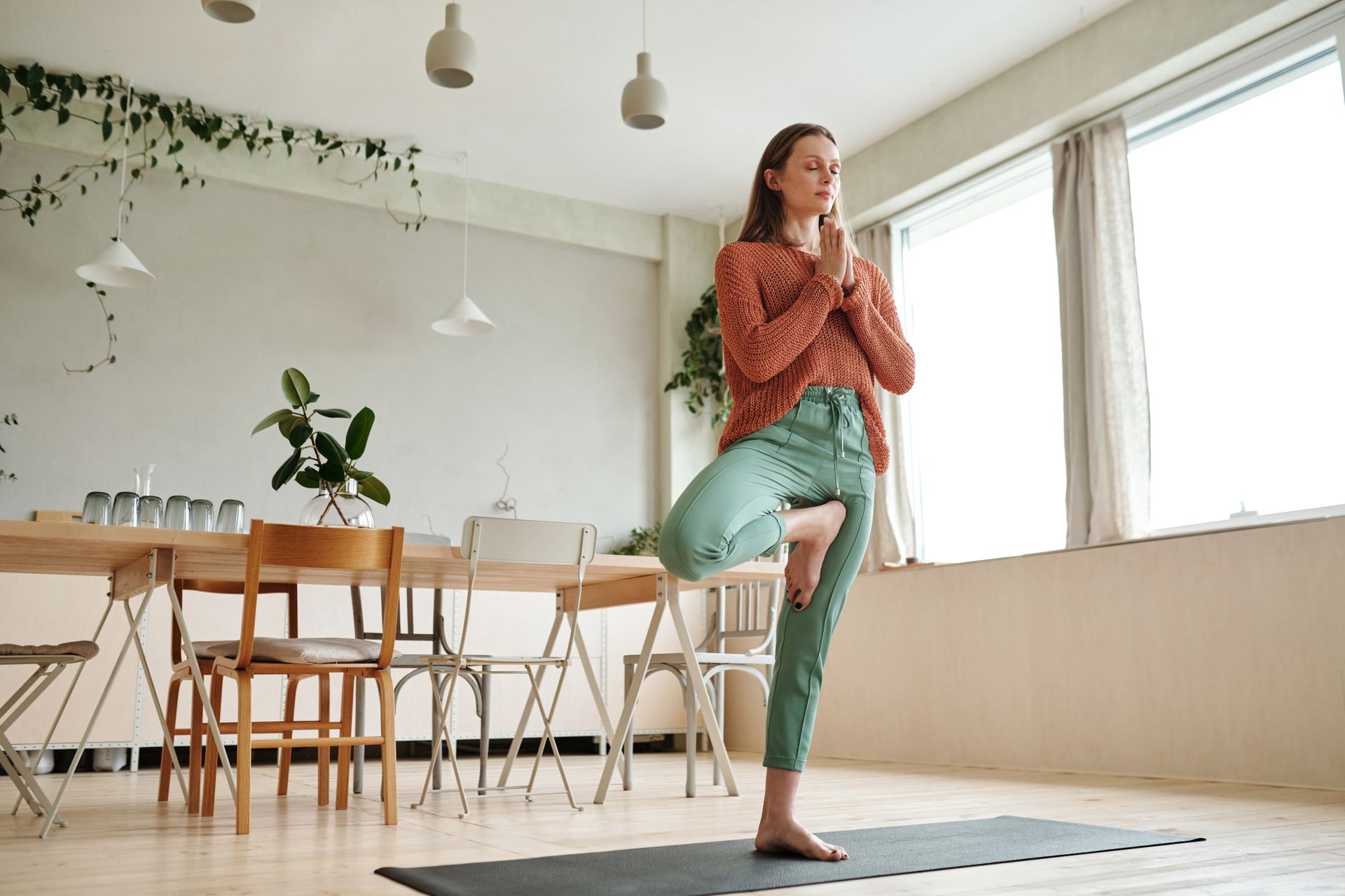 A woman practices yoga on a mat in her sunlit dining room, embracing mindfulness and balance.