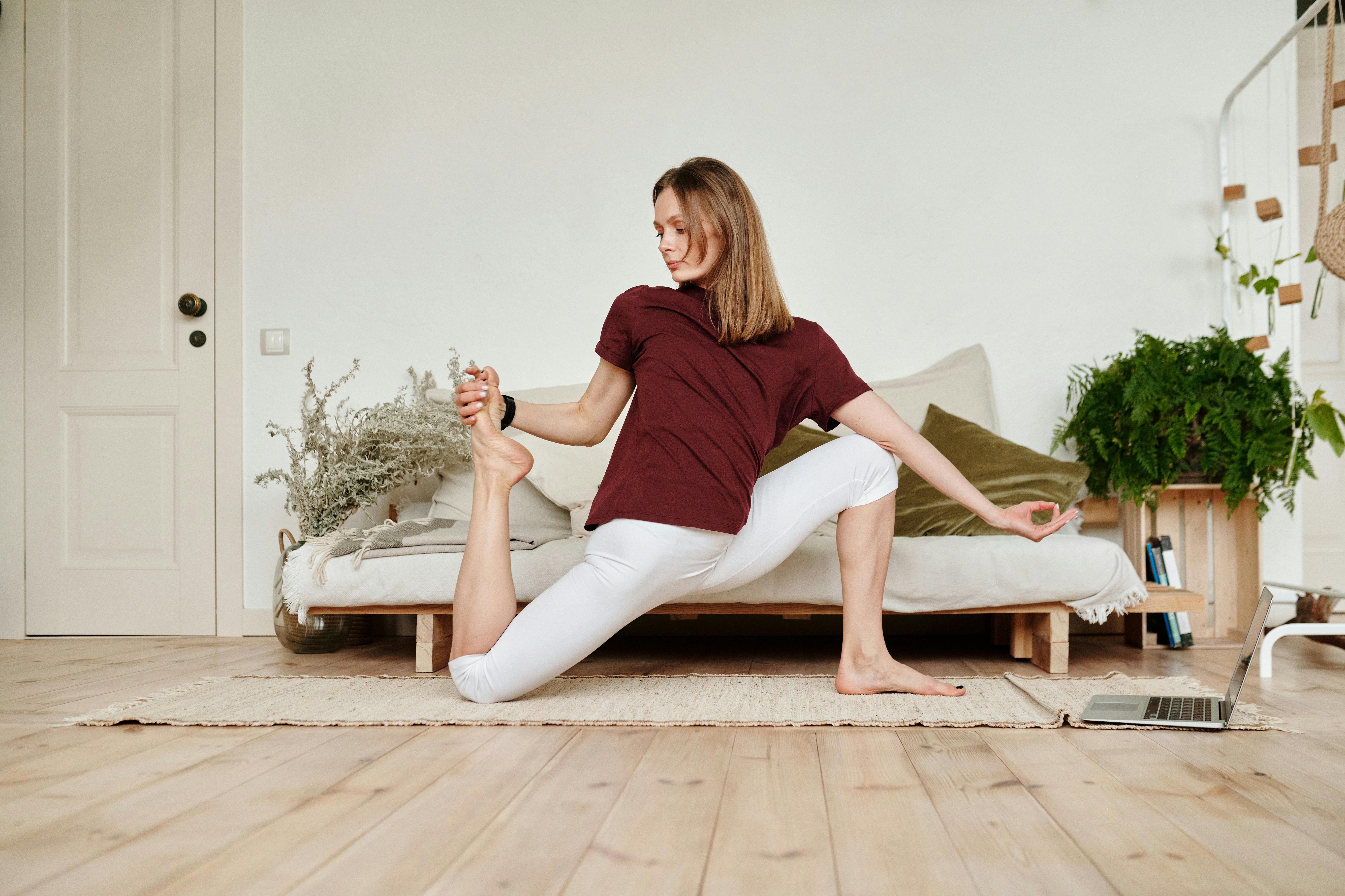 Young woman doing yoga indoors with a laptop nearby, embracing a flexible lifestyle.