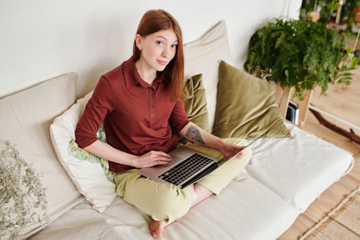 Woman sitting on sofa working remotely on a laptop, enjoying a comfortable home setting.