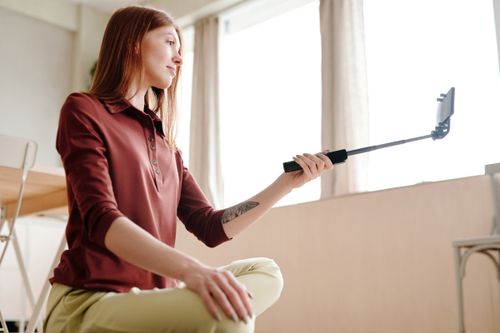 Free Young woman recording a vlog indoors using a selfie stick. Natural light and casual setting. Stock Photo