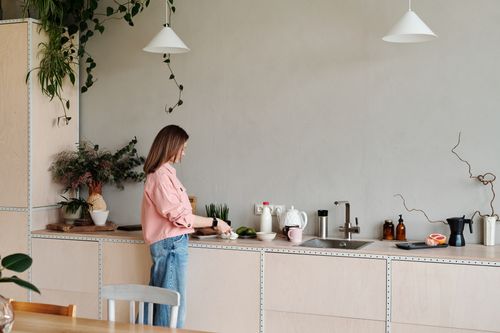 Free A woman in a pink shirt slices vegetables in a stylish minimalist kitchen with houseplants. Stock Photo