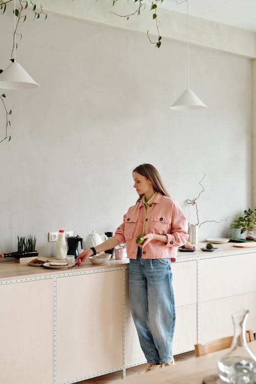 Mulher Em Camisa De Manga Comprida Rosa E Jeans Azul Em Pé Ao Lado Da Mesa De Madeira Branca