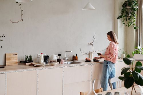Free Woman slicing avocados on a stylish kitchen counter with plants around. Bright indoor setting. Stock Photo