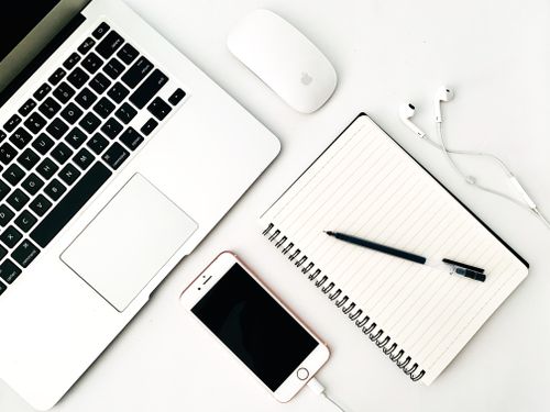 Free Top view black and white of modern netbook with wireless mouse near cellphone with charger and blank notepad with pen near earphones on desk in office Stock Photo
