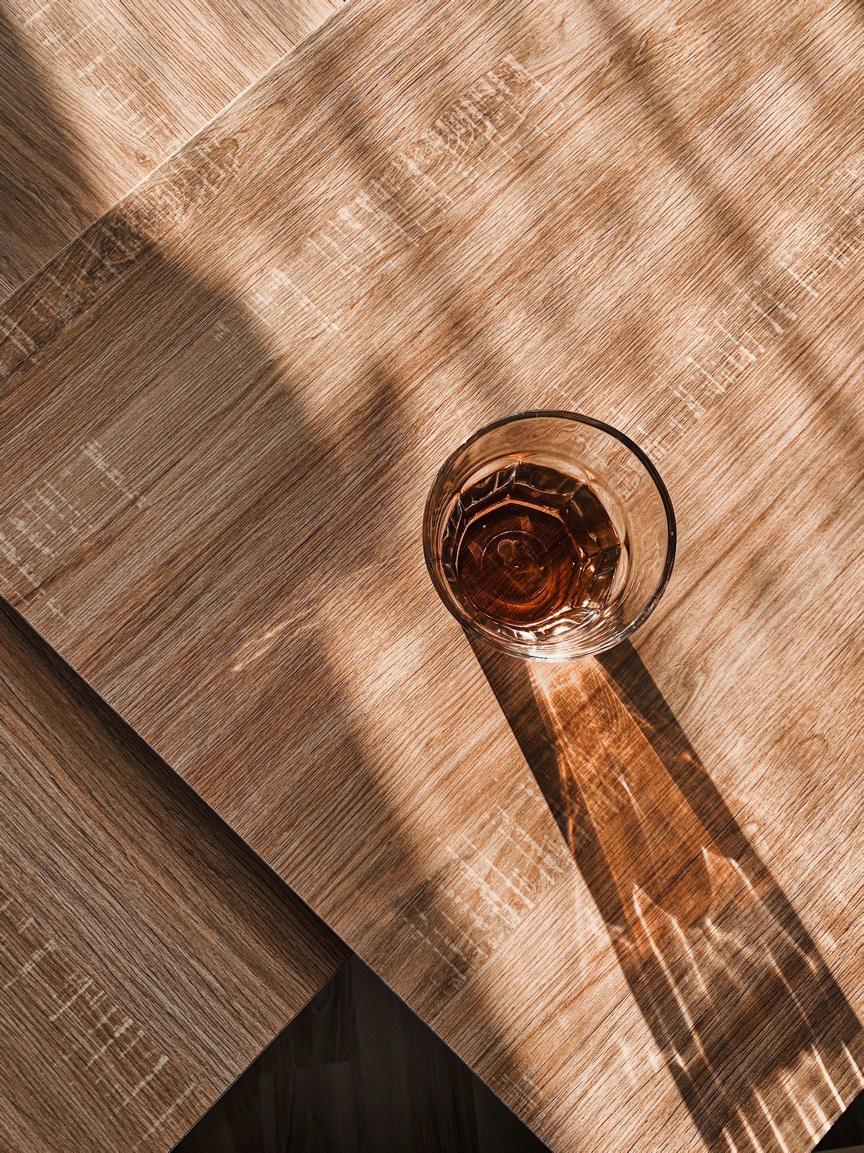 From above of transparent glass with beverage placed on wooden table and illuminated by sunlight