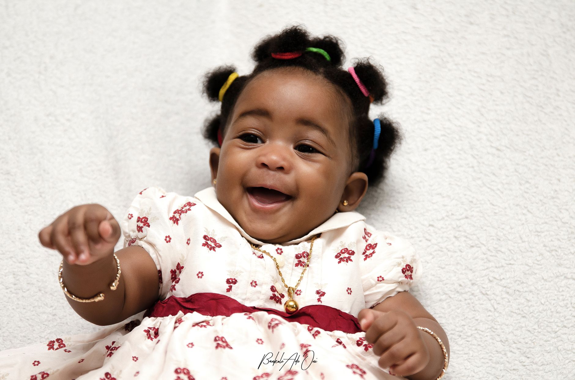 A joyful baby girl with colorful hair ties smiling indoors, captured in Nigeria.