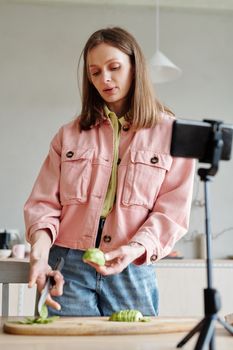 Woman slicing an avocado while vlogging in a cozy kitchen setup.