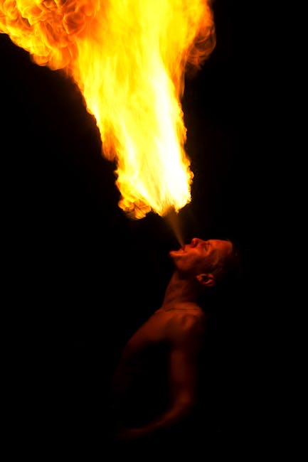 A performer showcasing a dramatic fire breathing stunt against a dark backdrop at night.