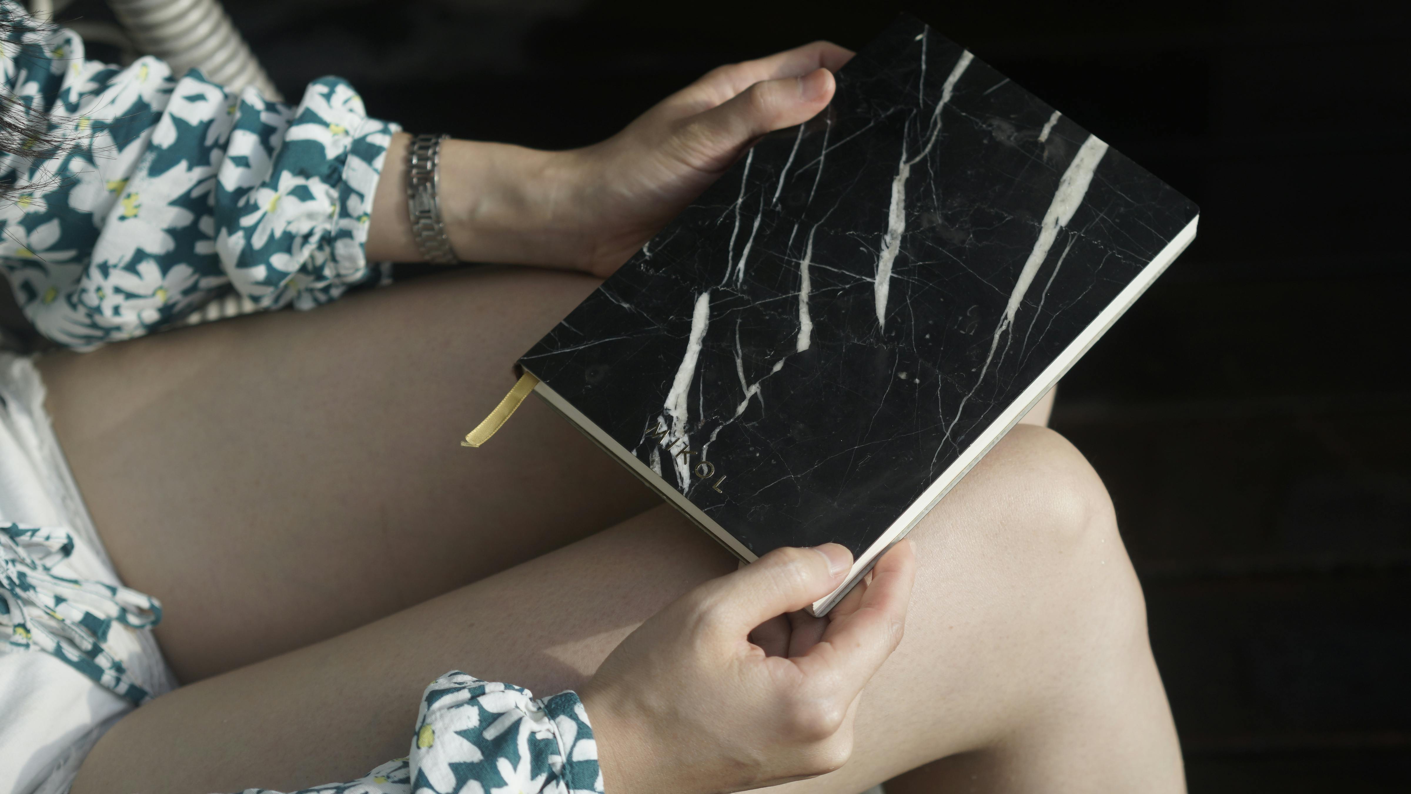 A woman holds a stylish marble-design notebook on her lap, ready to write.
