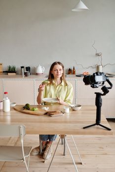 Woman filming avocado toast tutorial at home in modern kitchen for vlog.