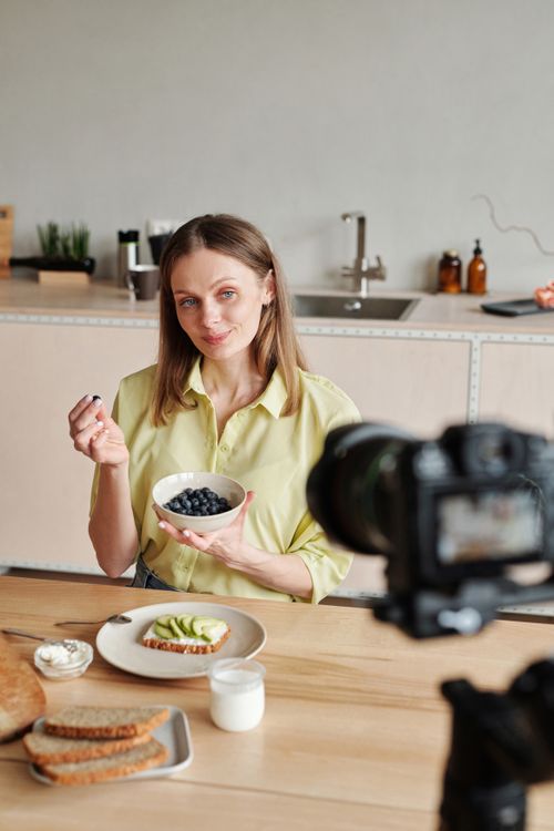 Free A woman films a vlog about healthy breakfast options with blueberries and avocado toast. Stock Photo