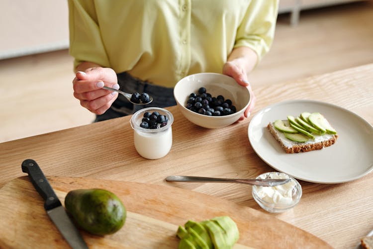 Person Putting Blueberries On Yogurt 