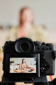 A woman vlogs a cooking session in her kitchen, captured through a camera viewfinder.