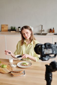 Woman prepares and films breakfast vlog with blueberries and avocado toast.
