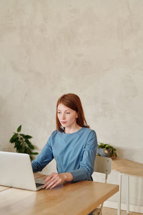 Free Brunette woman in blue sweater works on a laptop at home. Cozy indoor setting. Stock Photo