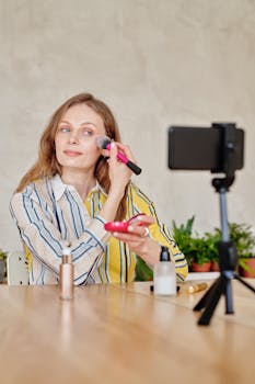 Caucasian woman vlogging makeup tutorial indoors with makeup brush and cosmetics.
