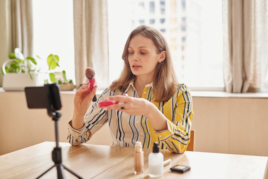 A woman demonstrating makeup techniques for a vlog using cosmetics at home.