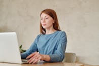 一位穿着蓝色衬衫的白人妇女正在家中用笔记本电脑工作