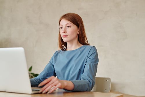 Free Caucasian woman in blue shirt working on a laptop indoors at home. Stock Photo