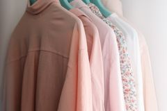 Modern shirts of different pink color shades on plastic hangers with metal hooks hanging on wooden beam in wardrobe near white concrete wall in apartment