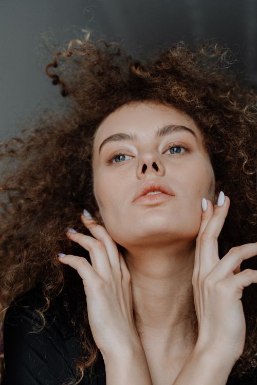 Free Close-up portrait of a young woman with natural curls and captivating eyes, exuding elegance and beauty. Stock Photo