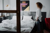 一位女士站在一间舒适的卧室里，卧室充满现代艺术气息，展现了舒适而时尚的内饰