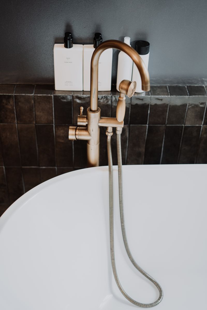 Brass bathtub filler against dark tiles
