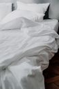 现代卧室环境中，一张舒适的白色亚麻床的特写镜头，床上的用品有些皱巴巴的