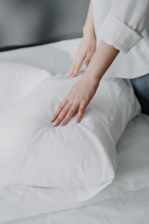 Free Person in White Shirt and Gray Denim Jeans Sitting on White Bed Stock Photo