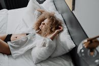 一位卷发女子身着白衬衫，在舒适且阳光明媚的卧室里放松身心