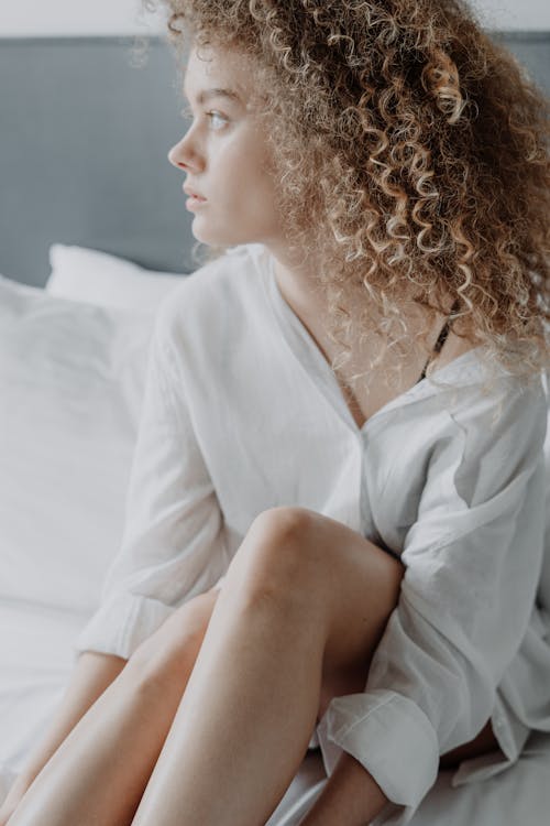 Free Woman in White Dress Shirt Sitting on White Bed Stock Photo