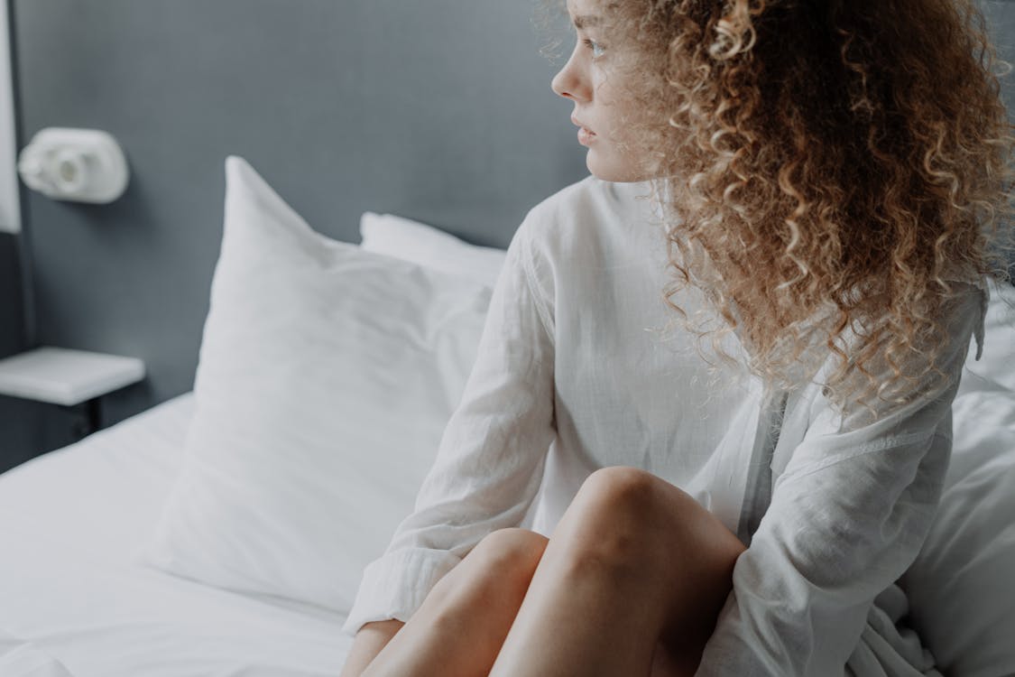 Free Woman in White Long Sleeve Shirt Sitting on Bed Stock Photo